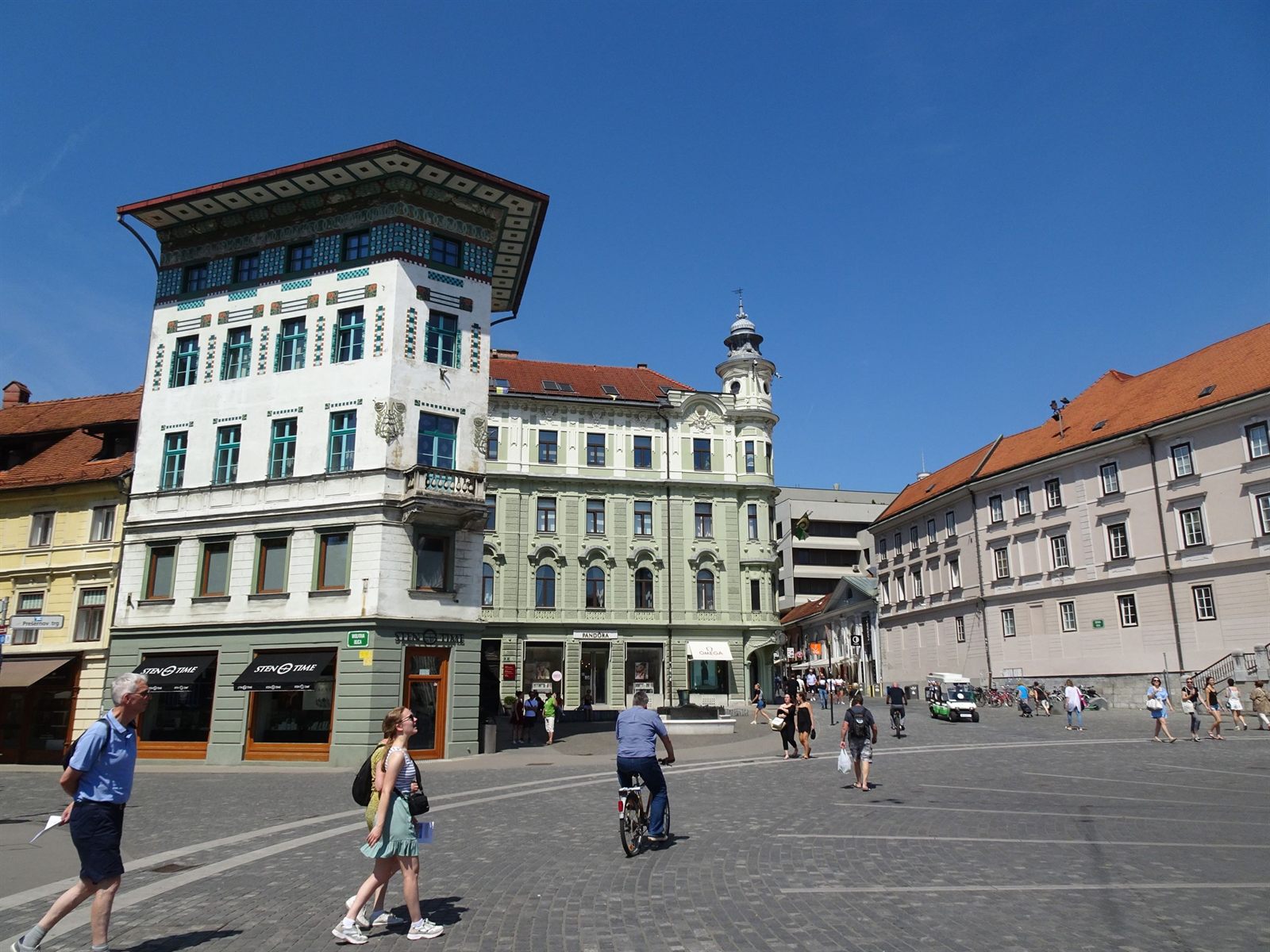People walking and cycling across a sunny old-town square in Ljubljana, Slovenia