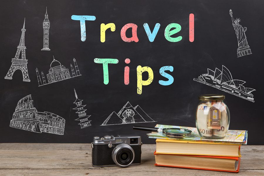 Chalkboard reading Travel Tips beside a camera and books